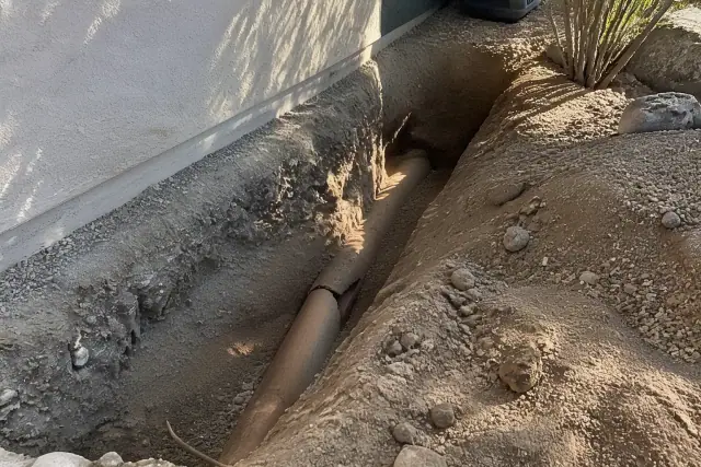 Deep trench showing cracked sewer pipe repair in progress at a residential foundation in Goodyear, AZ.
