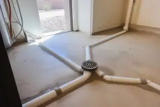 Finished sewer line repair with intersecting PVC pipes and a central floor drain in a Phoenix, AZ utility room.