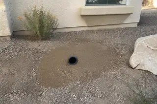 Finished pipe bursting project showing a backfilled access pit and new HDPE pipe end in a Phoenix, AZ yard.