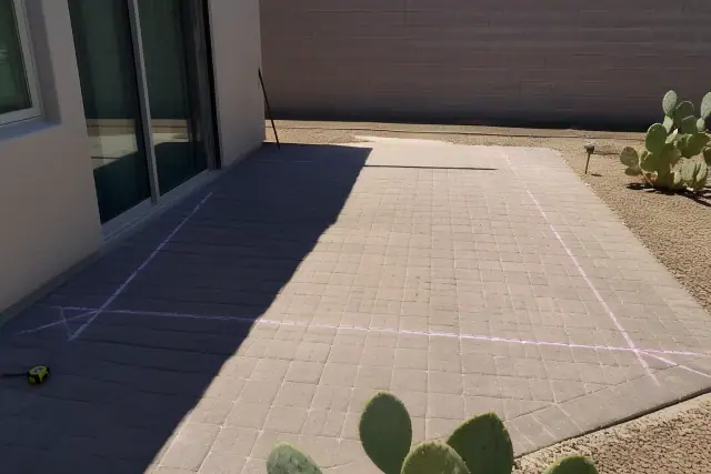 Chalk lines marking a shade sail footprint on a stone patio in Phoenix, AZ with prickly pear cactus and crushed granite.
