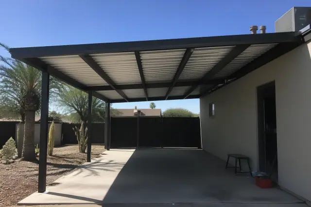 Attached carport installation over a concrete driveway in Phoenix, AZ with metal beams and desert landscaping.