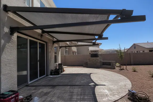 Cantilever shade structure with fabric canopy over a stone patio in a residential backyard in Queen Creek, AZ.