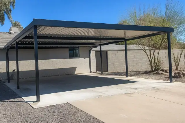 A finished metal carport installed over a concrete driveway pad on a sunny day in Phoenix, AZ.