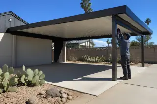 Technician checking metal joints of a carport on a concrete slab in a Phoenix, AZ backyard with prickly pear cacti.