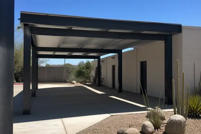 Commercial carport with steel beams and metal roofing over a concrete slab at a Phoenix, AZ worksite with desert plants.