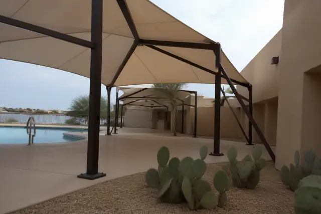 Commercial shade structures installed on a pool deck with steel mounting plates and desert landscaping in Peoria, AZ.