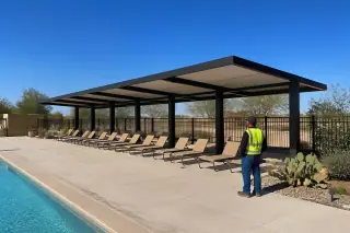 Professional checking a steel shade canopy over a poolside lounge area in a Phoenix, AZ commercial backyard.