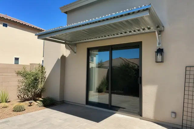Galvanized steel awnings mounted over a paved patio next to a sliding glass door in a Phoenix, AZ backyard.