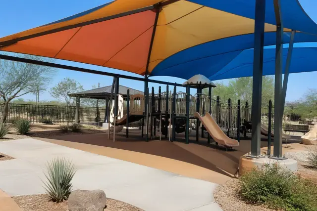 Fabric shade structure over a playground with climbing equipment in a fenced park in Phoenix, AZ.