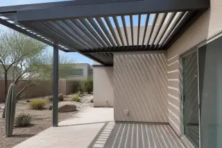 Adjustable louvered roof with metallic slats over a stone patio and desert cacti in a Phoenix, AZ backyard.