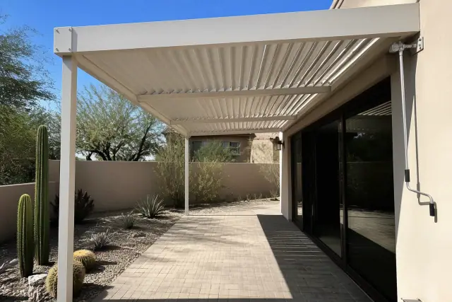 Louvered roof system installed over a stone patio in Phoenix, AZ, with xeric landscaping and stucco walls.