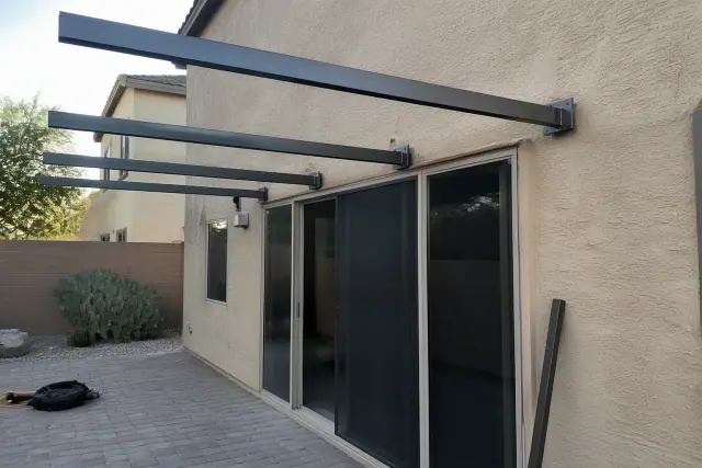 Metal awning installation with steel brackets and support rafters on a residential patio in Peoria, AZ.