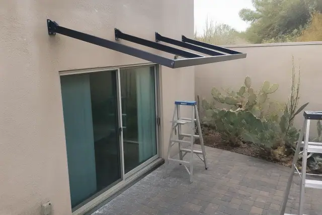 Metal awning installation with steel brackets over a sliding glass door at a paved patio in Tempe, AZ.