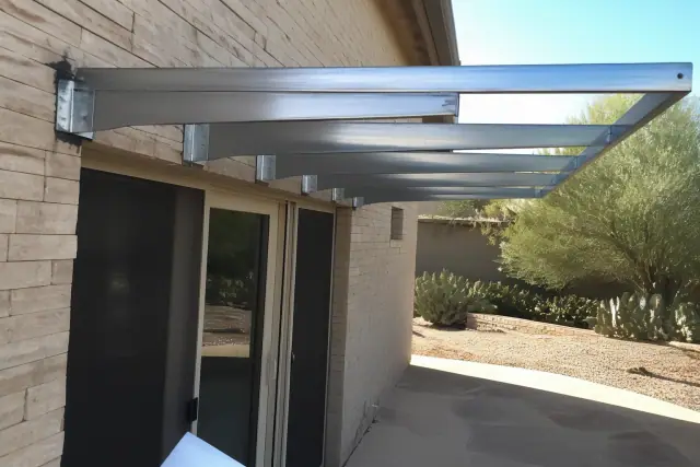 Metal awning installation over a residential backyard patio in Glendale, AZ with steel brackets bolted to a stone wall.