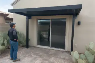 Contractor inspecting a metal awning above a stone patio with prickly pear cactus in a Phoenix, AZ backyard.