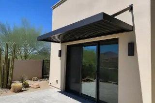 Metal awning attached to a stucco wall above sliding glass doors in a Phoenix, AZ backyard with desert landscaping.