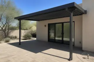 Completed metal awning casting a shadow over a stone patio with stucco walls in a Phoenix, AZ backyard.
