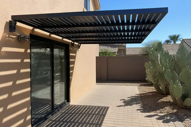 Metal awning installed over a paved patio door in a Phoenix, AZ backyard with desert landscaping.