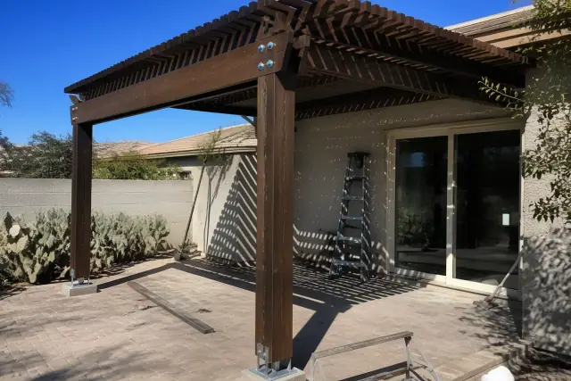 A pergola structure being installed over a backyard stone patio with prickly pear cactus in Phoenix, AZ.