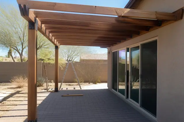 Cedar pergola rafters and steel mounting brackets being installed on a paved residential patio in Chandler, AZ.