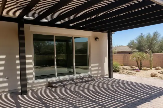Pergola slats filtering sunlight over a paved patio area next to a sliding glass door in Phoenix, AZ.