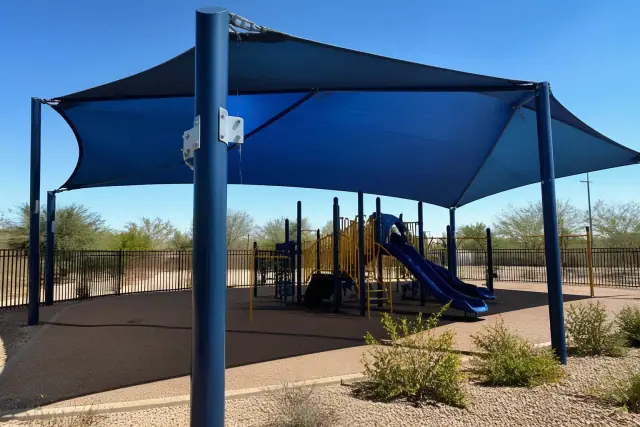 Tensioned fabric shade structures over a playground in a xeriscaped recreational area in Peoria, AZ.