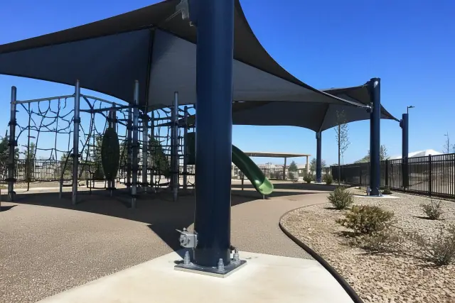 Playground shade structures installed at a public park in Chandler, AZ, showing steel mounting bolts in concrete.