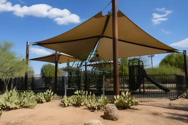 Commercial shade structures with fabric canopies over a playground in Phoenix, AZ, surrounded by desert soil and cacti.