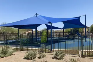 Large fabric shade canopy over a playground with prickly pear cacti in a Phoenix, AZ park.