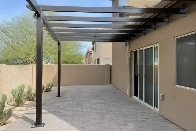 Steel shade structure frame with overhead beams bolted to stone pavers on a residential patio in Tempe, AZ.