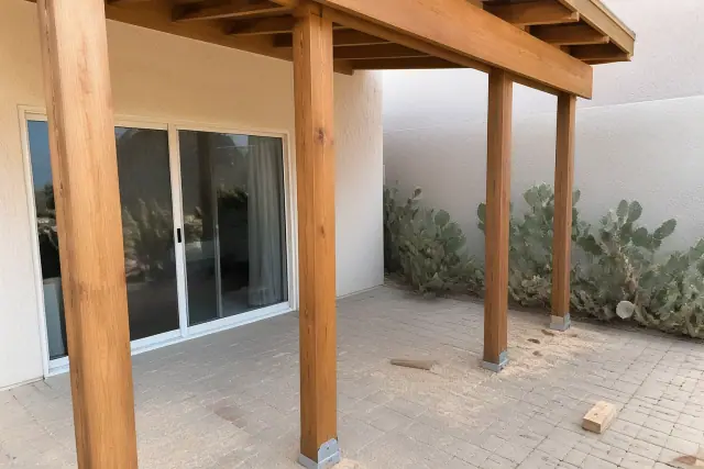 Wooden shade structure support beams installed on a stone patio in Glendale, AZ with prickly pear cactus nearby.