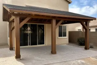 Wooden ramada with timber posts and shingle roof over a stone patio in a Phoenix, AZ backyard with desert landscaping.