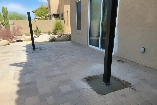 Shade-sail footings installed at a paved stone patio near a sliding glass door in Phoenix, AZ.