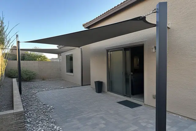 Shade sail installation over a residential backyard patio in Gilbert, AZ, featuring steel posts and stone paving.