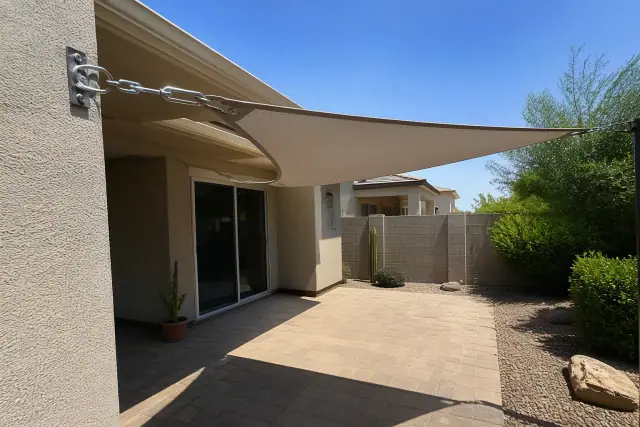Shade sail installed over a paved patio in a residential backyard in Phoenix, AZ, showing mounting hardware and fabric.