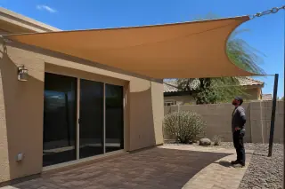 Technician inspecting a shade sail installed over a stone patio in a Phoenix, AZ backyard with xeriscape landscaping.