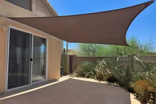 Taut shade sail fabric anchored above a stone patio near prickly pear cactus in a Phoenix, AZ backyard.