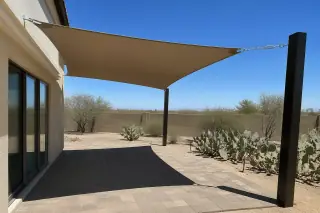 Shade sail mounted with stainless steel hardware over a stone patio in a Phoenix, AZ backyard with prickly pear cacti.