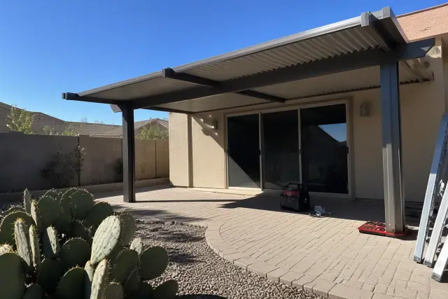 Standard aluminum cover being installed over a stone patio in a Phoenix, AZ backyard with desert landscaping.