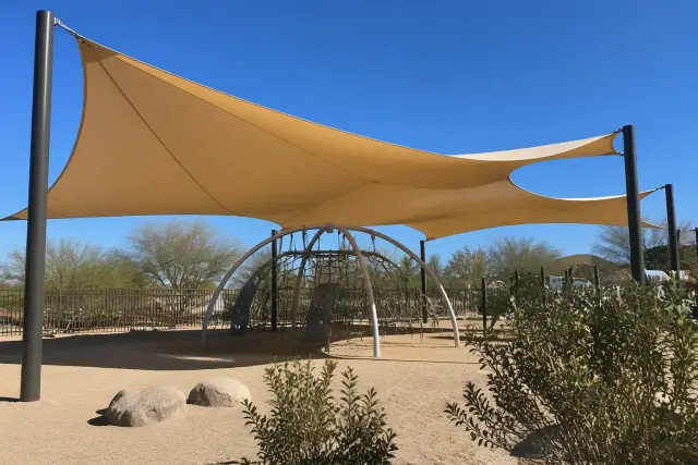Tensioned fabric shade sails over a playground in Phoenix, AZ, with steel support posts and desert landscaping.