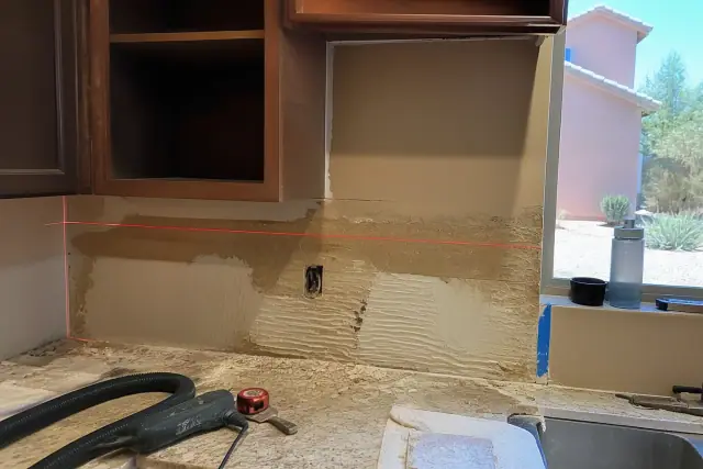 In-progress kitchen backsplash removal with exposed wall substrate and laser level in a Phoenix, AZ home.