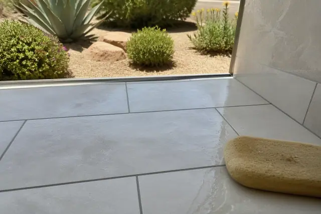 Damp sponge wiping excess grout from newly installed stone bathroom floor tiles in Phoenix, AZ.