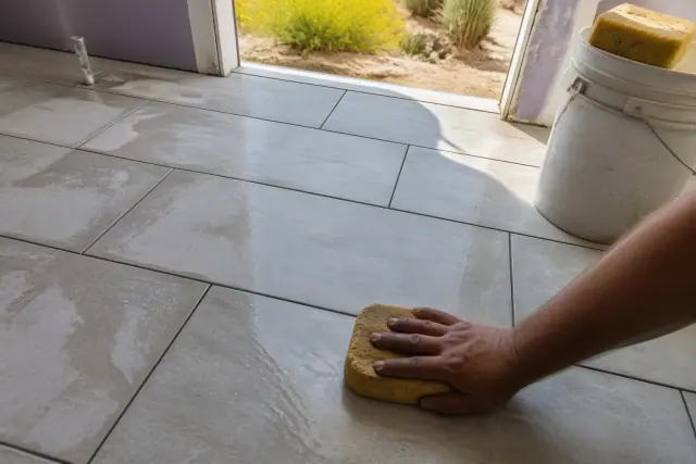 Technician wiping grout from new stone tile flooring in a home in Mesa, AZ.