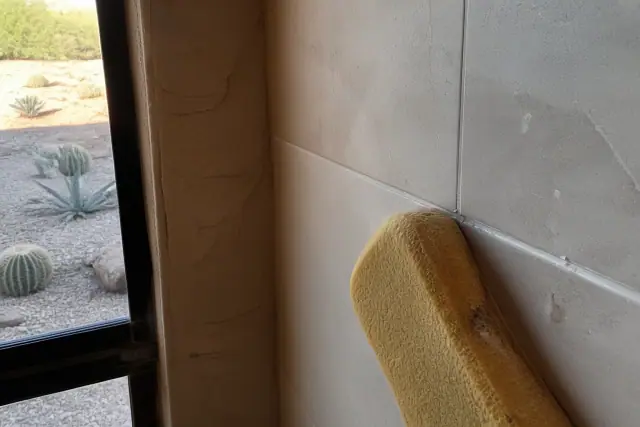 A damp sponge wiping excess mortar from newly installed shower tiles in a home in Phoenix, AZ.