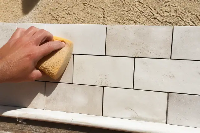 Damp sponge cleaning fresh mortar from a stone tile kitchen backsplash during an installation in Phoenix, AZ.