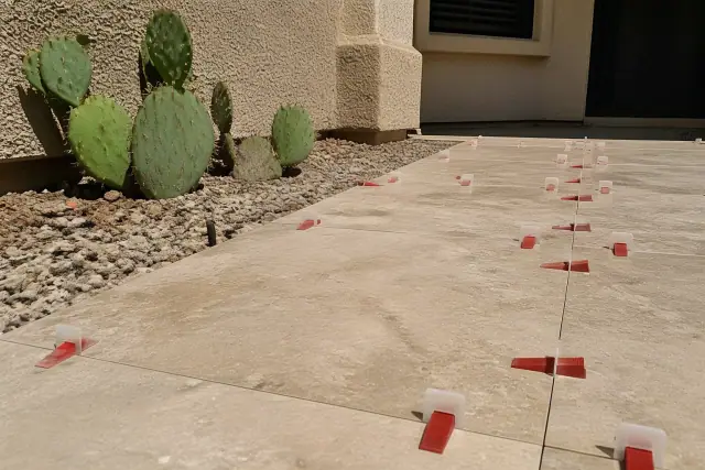 Plastic leveling clips and tiles installed on a patio in Phoenix, AZ, with desert landscaping nearby.