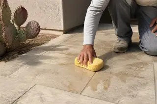 Contractor wiping excess mortar from new stone tile grout lines at a Phoenix, AZ jobsite with desert landscaping.