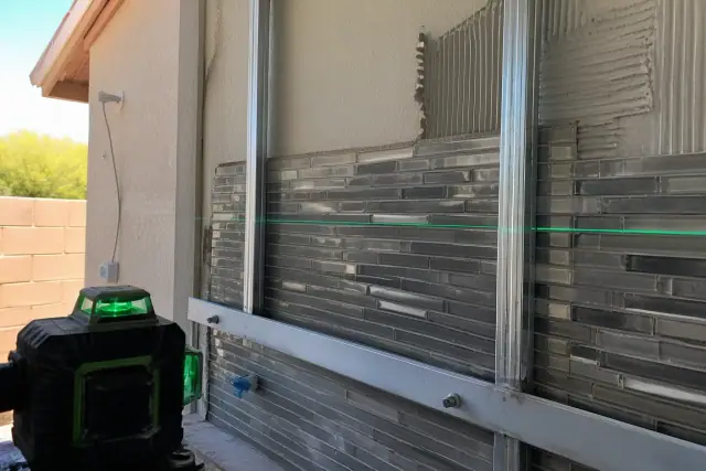 Glass and mosaic tile kitchen backsplash installation with a laser level beam on a jobsite in Phoenix, AZ.