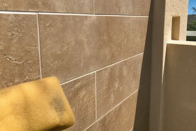Damp sponge wiping excess mortar from between stone shower tiles during a renovation project in Phoenix, AZ.