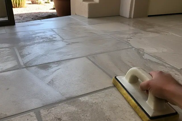 Technician using a sponge to clean fresh grout from stone floor tiles in a home in Peoria, AZ.